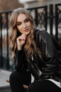 Kentin arka planında siyah deri ceketli, gülümseyen güzel sarışın bir kadının portresini yakından çek.