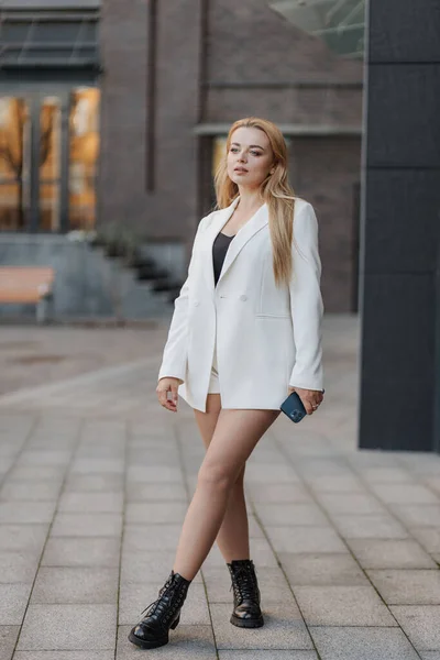 Blond Stijlvolle Vrouw Oversized Witte Jas Met Behulp Van Telefoon — Stockfoto