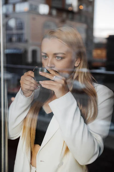 stock image Blond stylish woman at oversized white jacket drinking aroma coffee and relax at cafe