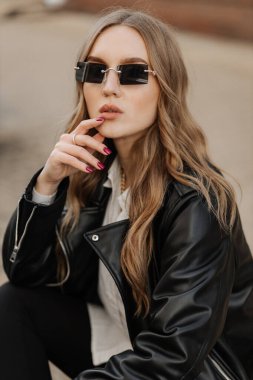 Kentin arka planında siyah deri ceketli, gülümseyen güzel sarışın bir kadının portresini yakından çek.