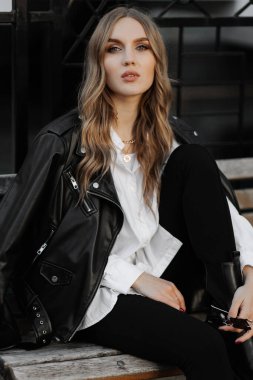 Kentin arka planında siyah deri ceketli, gülümseyen güzel sarışın bir kadının portresini yakından çek.