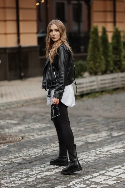 时尚的金发女模特 身穿黑色皮夹克 头戴时尚手提包 走在城市街道上 — 图库照片