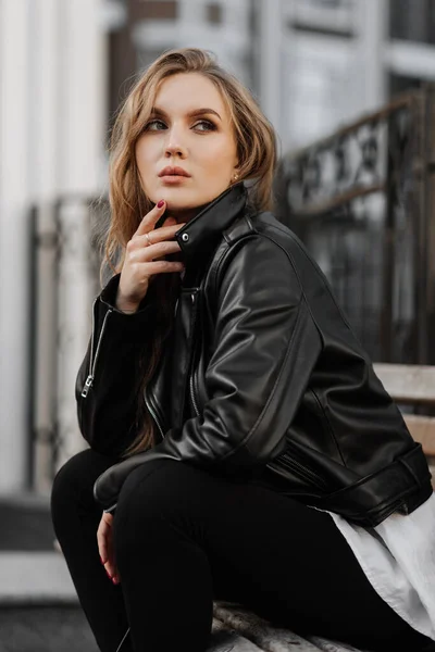 在城市街道背景上 一个身穿黑色皮夹克的漂亮的金发年轻女子的近照 — 图库照片