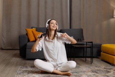 Genç kız kulaklık takıyor, akıllı telefon kullanıyor ve evde online video kursu izliyor.