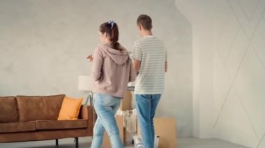 Yeni Evde Yürüyen Genç Bir Çift Son Şeyleri Getiriyorlar. Çift yeni evi tartışıyor. Mutlu çift kanepeye oturup dinleniyor. Televizyon ve Çiçek Taşıyan Adam.
