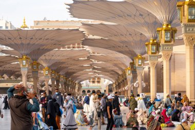 Medine, Suudi Arabistan - 18 Aralık 2024: Medine 'deki Büyük Kral Abdullah Camii' nin dev şemsiyeleri altındaki hacılar, Suudi Arabistan 'ın ikinci en kutsal İslam mekanı.