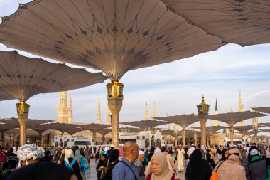 Medine, Suudi Arabistan - 18 Aralık 2024: Medine 'deki Büyük Kral Abdullah Camii' nin dev şemsiyeleri altındaki hacılar, Suudi Arabistan 'ın ikinci en kutsal İslam mekanı.