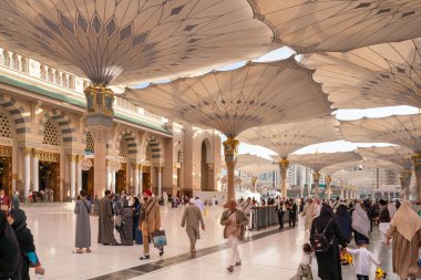 Medine, Suudi Arabistan - 18 Aralık 2024: Medine 'deki Büyük Kral Abdullah Camii' nin dev şemsiyeleri altındaki hacılar, Suudi Arabistan 'ın ikinci en kutsal İslam mekanı.