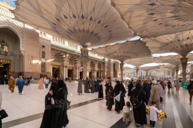 Medine, Suudi Arabistan - 18 Aralık 2024: Medine 'deki Büyük Kral Abdullah Camii' nin dev şemsiyeleri altındaki hacılar, Suudi Arabistan 'ın ikinci en kutsal İslam mekanı.