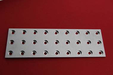 Kırmızı yüzeyinde delikleri olan metal bir plaka.