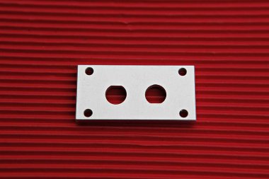 Kırmızı zemin üzerinde iki deliği olan metal bir plaka.
