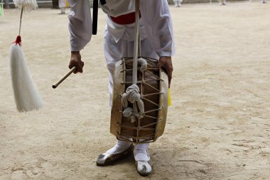 Elinde davul ve beyaz tüy tutan beyaz elbiseli bir adam.