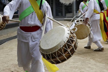 Bir grup beyaz elbiseli adam davul çalıyor.