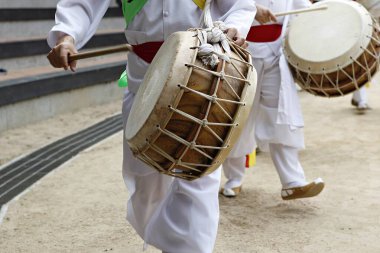 Bir grup beyaz elbiseli adam davul çalıyor.