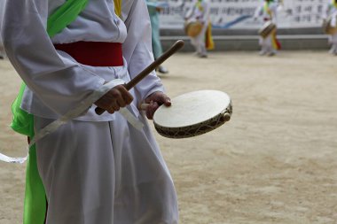 Elinde davul ve sopa tutan beyaz elbiseli bir adam.
