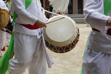 Bir grup beyaz ve yeşil kıyafetli adam davul çalıyor.