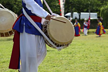 Mavi ve kırmızı kıyafetli bir adam davul çalıyor.