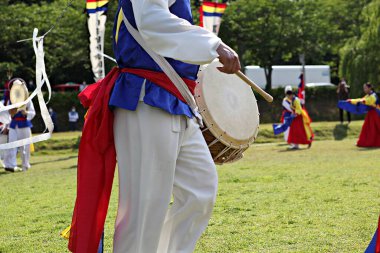 Mavi ve kırmızı kıyafetli bir adam davul çalıyor.