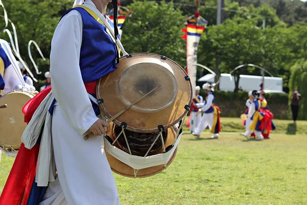 Mavi beyaz kıyafetli bir adam davul çalıyor.