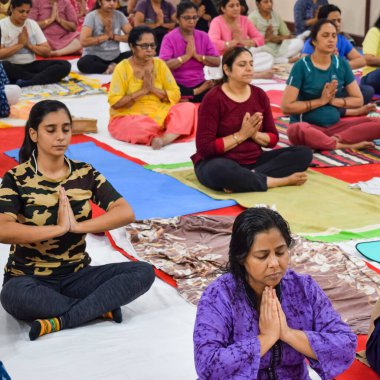 New Delhi, India, June 19 2022 -Group Yoga exercise session for people of different age groups in Balaji Temple, Vivek Vihar, International Yoga Day, Big group of adults attending yoga class in temple