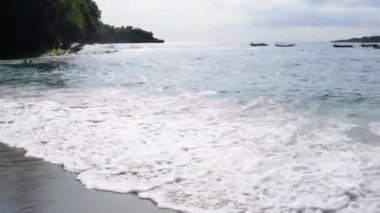 Gün batımında Crystal Körfezi 'nin manzaralı okyanus koyunda. Çarpışan dalgalar, demirlemiş tekneler, renkli günbatımı, Endonezya 'nın Bali kentinin güneydoğusundaki bir ada olan Nusa Penida' nın batı kıyısında bulunan tropikal titreşimler.