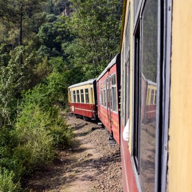 Oyuncak tren dağ yamaçlarında hareket ediyor, güzel bir manzara, bir dağ yamacı, bir vadi yamaçtan tepeye hareket ediyor, yeşil doğal ormanın arasında. Hindistan 'da Kalka' dan Shimla 'ya giden oyuncak tren, Hint treni.