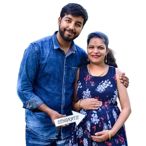 Indian couple posing for maternity baby shoot with white plain background. The couple is posing in a lawn with green grass and the woman is falunting her baby bump in Lodhi Garden in New Delhi, India