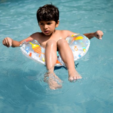 Havuzda yüzen mutlu Hintli çocuk, sıcak yaz tatillerinde hava tüpüyle birlikte yüzen çocuk, büyük bir havuzda yüzen çocuk..