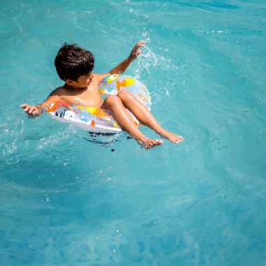 Havuzda yüzen mutlu Hintli çocuk, sıcak yaz tatillerinde hava tüpüyle birlikte yüzen çocuk, büyük bir havuzda yüzen çocuk..