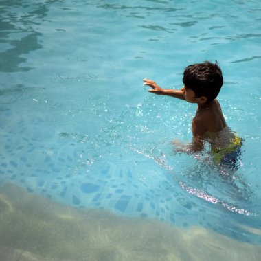 Havuzda yüzen mutlu Hintli çocuk, sıcak yaz tatillerinde hava tüpüyle birlikte yüzen çocuk, büyük bir havuzda yüzen çocuk..