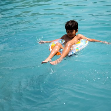 Havuzda yüzen mutlu Hintli çocuk, sıcak yaz tatillerinde hava tüpüyle birlikte yüzen çocuk, büyük bir havuzda yüzen çocuk..