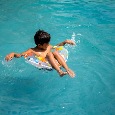 Havuzda yüzen mutlu Hintli çocuk, sıcak yaz tatillerinde hava tüpüyle birlikte yüzen çocuk, büyük bir havuzda yüzen çocuk..