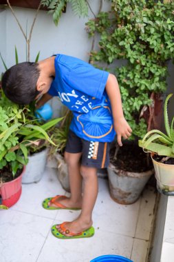 Şirin 5 yaşındaki Asyalı çocuk, ev balkonundaki saksıları suluyor. Bitkileri sularken küçük tatlı bir çocuğun doğaya olan sevgisi.