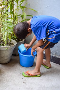 Şirin 5 yaşındaki Asyalı çocuk, ev balkonundaki saksıları suluyor. Bitkileri sularken küçük tatlı bir çocuğun doğaya olan sevgisi.