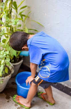 Şirin 5 yaşındaki Asyalı çocuk, ev balkonundaki saksıları suluyor. Bitkileri sularken küçük tatlı bir çocuğun doğaya olan sevgisi.