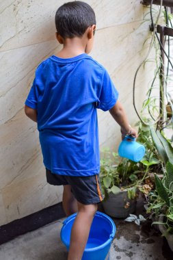 Şirin 5 yaşındaki Asyalı çocuk, ev balkonundaki saksıları suluyor. Bitkileri sularken küçük tatlı bir çocuğun doğaya olan sevgisi.