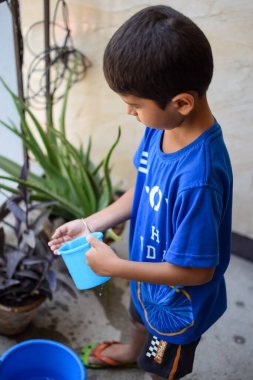 Şirin 5 yaşındaki Asyalı çocuk, ev balkonundaki saksıları suluyor. Bitkileri sularken küçük tatlı bir çocuğun doğaya olan sevgisi.