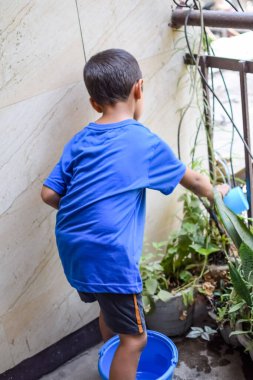 Şirin 5 yaşındaki Asyalı çocuk, ev balkonundaki saksıları suluyor. Bitkileri sularken küçük tatlı bir çocuğun doğaya olan sevgisi.