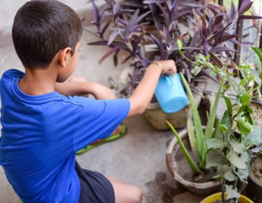 Şirin 5 yaşındaki Asyalı çocuk, ev balkonundaki saksıları suluyor. Bitkileri sularken küçük tatlı bir çocuğun doğaya olan sevgisi.