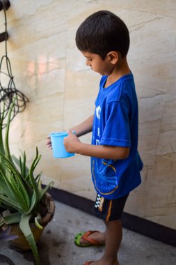 Şirin 5 yaşındaki Asyalı çocuk, ev balkonundaki saksıları suluyor. Bitkileri sularken küçük tatlı bir çocuğun doğaya olan sevgisi.