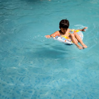 Havuzda yüzen mutlu Hintli çocuk, sıcak yaz tatillerinde hava tüpüyle birlikte yüzen çocuk, büyük bir havuzda yüzen çocuk..