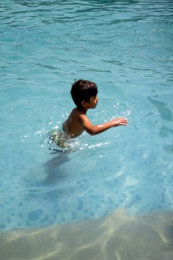 Havuzda yüzen mutlu Hintli çocuk, sıcak yaz tatillerinde hava tüpüyle birlikte yüzen çocuk, büyük bir havuzda yüzen çocuk..