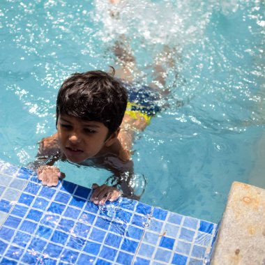 Havuzda yüzen mutlu Hintli çocuk, sıcak yaz tatillerinde hava tüpüyle birlikte yüzen çocuk, büyük bir havuzda yüzen çocuk..