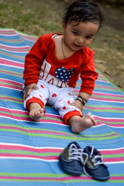 Delhi 'deki sosyete parkında oturup eğlenen şirin küçük Hintli bebek, etrafta çimen olan renkli minder üzerinde oturan sevimli bebek, dışarıda ateş eden bebek.