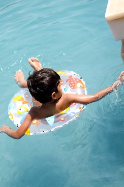 Havuzda yüzen mutlu Hintli çocuk, sıcak yaz tatillerinde hava tüpüyle birlikte yüzen çocuk, büyük bir havuzda yüzen çocuk..