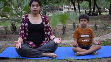 Çocuğuyla parkta yoga yapan Hintli genç bir kadın. Oğluyla güzel bir kız, temel yoga pozu veriyor. Sakin ol ve rahatla, kadın mutluluğu. Yoga pozları. 