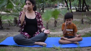 Çocuğuyla parkta yoga yapan Hintli genç bir kadın. Oğluyla güzel bir kız, temel yoga pozu veriyor. Sakin ol ve rahatla, kadın mutluluğu. Yoga pozları. 