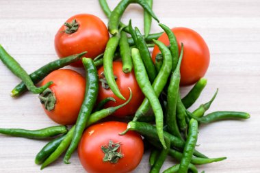 Sade ahşap masada kırmızı domates ve yeşil biber, tüm temel gıdalar için yeşil sebze, sade arka planda soyulmamış sebze manzarası