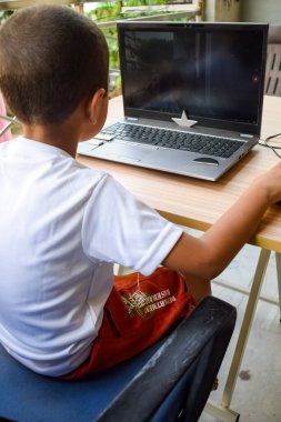 1. sınıftaki dizüstü bilgisayarını kullanan küçük bir çocuk, uzaktan eğitim için bilgisayarında okuyan bir çocuk, okul çocuğu yaşam tarzı konsepti.