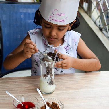 Tatlı Hintli aşçı kız vanilyalı dondurma, browni, kakao tozu, taze doğranmış meyve ve çilek şurubu içeren ateşte pişirilmemiş dondurma yemeğinin bir parçası olarak sundae hazırlıyor. Küçük çocuk yemek hazırlıyor.